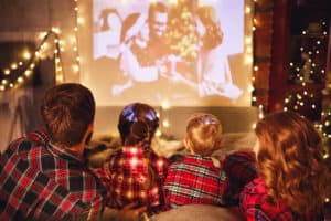 happy family in checkered pajamas: mother father and children watching projector, film, movies with popcorn in christmas holiday evening   at home
