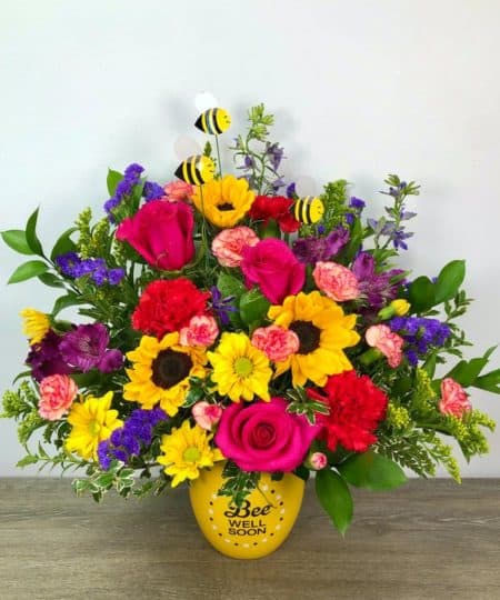 This vibrant cheery arrangement is the perfect pick-me-up gift. The designers use a variety of bright flowers with 3 bees buzzing around in a ceramic keepsake container. Approximately 17" height and 12" width
